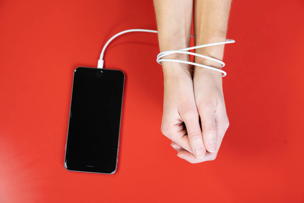 Woman's hands tied by the cord for charging a smartphone. - Foto, Bild
