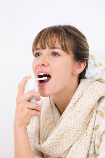 Молода жінка в ліжку страждає від болю в горлі з промиванням рота
. - Фото, зображення