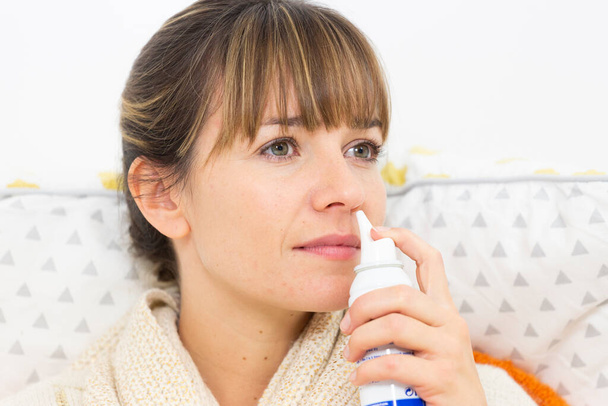 Молода жінка в ліжку страждає від застуди, з носовим розпилювачем
. - Фото, зображення