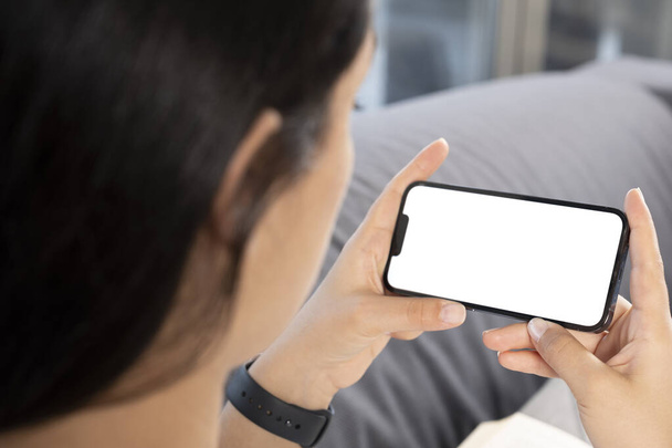 Smartphone mock up, close up over shoulder view of woman holding smartphone mock up. Young caucasian female looking white blank screen, watching video, online education or meeting concept idea photo. - 写真・画像