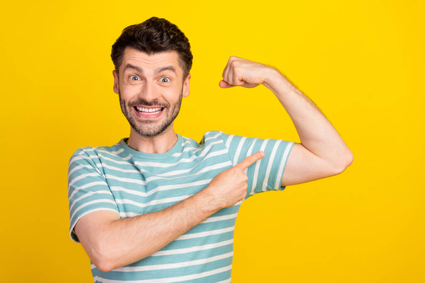 Photo of young attractive guy wear blue t-shirt showing biceps coach recommend gym isolated on yellow color background. - Photo, image