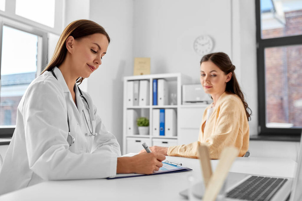medicine, healthcare and people concept - female doctor with clipboard talking to smiling woman patient at hospital - Foto, Imagen