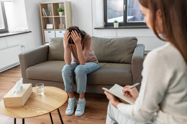 psychology, mental health and people concept - stressed young woman patient and psychologist at psychotherapy session - Foto, Bild