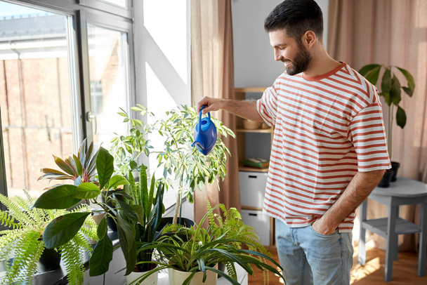 people, nature and plants care concept - happy smiling man watering flowers at home - Valokuva, kuva