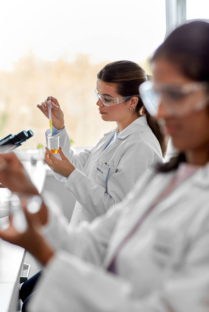 vědecký výzkum, práce a lidé koncept - ženský vědec s chemickým nebo zkušebním vzorkem v kádince a kapátkem pracující v laboratoři - Fotografie, Obrázek