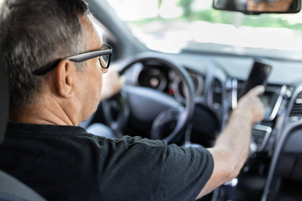 Senior behind the steering wheel using navigation and looking for directions - 写真・画像