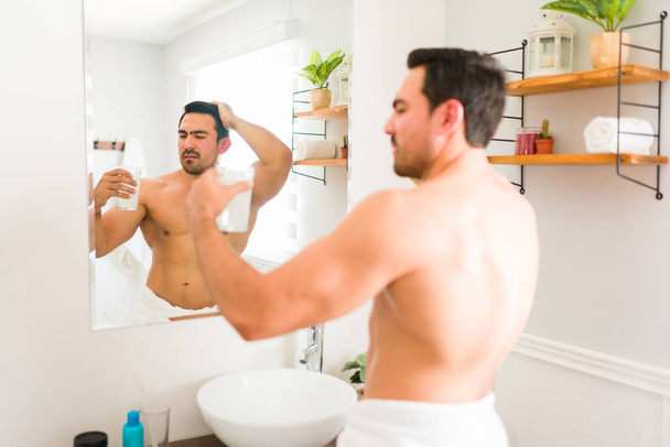 Stressed young man looking worried while taking a drink with vitamins or collagen while grooming and getting ready - Photo, image