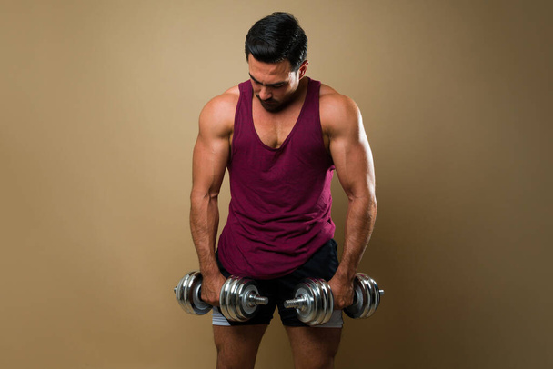 Fitness young man with a muscular body and biceps lifting dumbbell weights and doing a workout - Photo, image