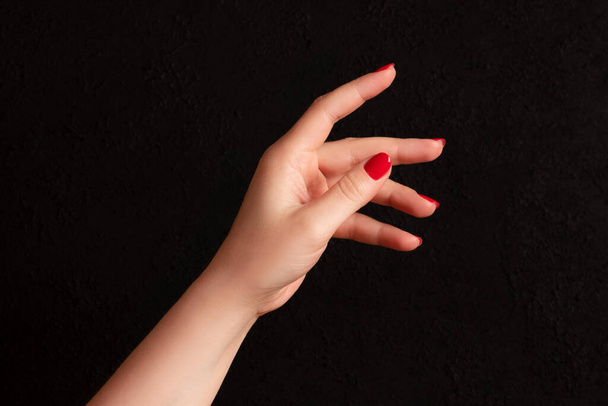 Main féminine avec une belle manucure - ongles rouges sur fond noir foncé - Photo, image