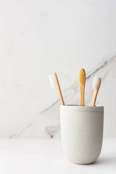 Cepillos de dientes de madera con cerdas naturales en un vaso de cerámica, productos naturales de higiene bucal - Foto, imagen