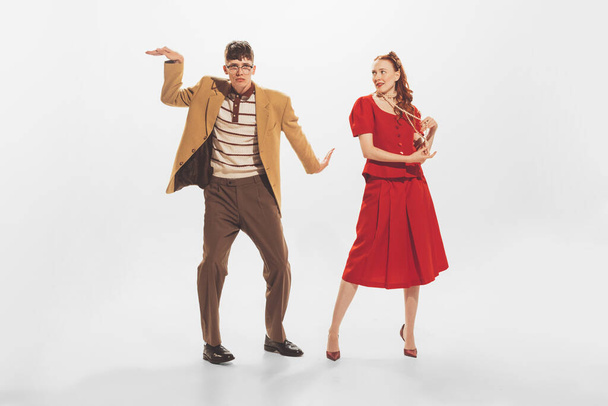 Portrait of stylish man in yellow jacket and beautiful woman in red dress dancing at retro party isolated over white background. Concept of retro fashion, style, youth culture, emotions, beauty, ad - 写真・画像