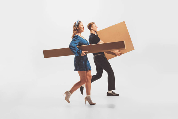 Young man and woman carrying big cardboard boxes isolated over white background. Black Friday shopping, sales, moving. Concept of retro fashion, style, youth culture, emotions, relationship, ad - Fotografie, Obrázek
