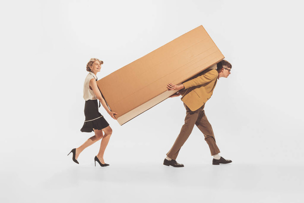 Young man and woman carrying big cardboard boxes isolated over white background. Black Friday shopping, sales, moving. Concept of retro fashion, style, youth culture, emotions, relationship, ad - Fotoğraf, Görsel