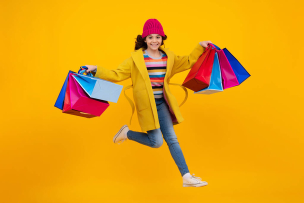 Girl teenager with shopping bags isolated on yellow backgound. Winter shopping sale. Run and jump. Happy teenager, positive and smiling emotions of teen girl - Foto, Imagem