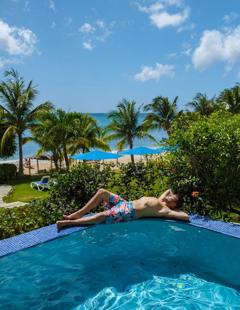 Young men in swim shorts sunbathing at Saint Lucia Caribbean, men at infinity pool during sunset. man in a swim shorts at the pool - Valokuva, kuva