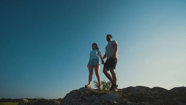 Молода пара стоїть на вершині гори на фоні блакитного неба
 - Фото, зображення