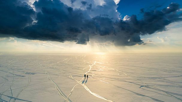 The two people with backpacks walking through the huge snow field - Photo, image