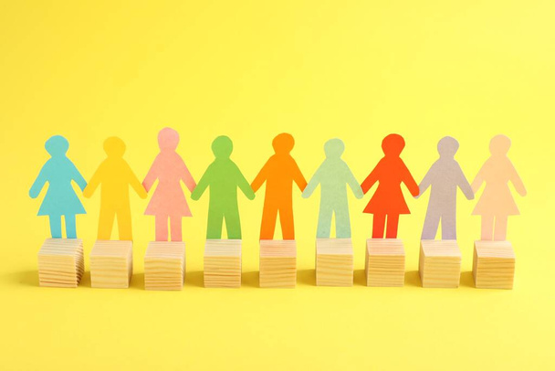 Paper human figures with wooden cubes on yellow background. Diversity and Inclusion concept - Foto, Imagem