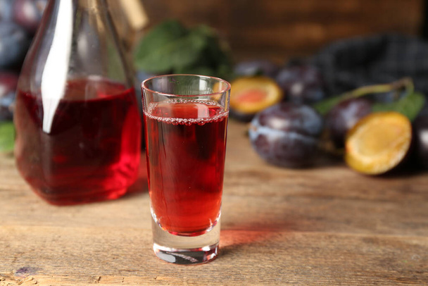 Delicious plum liquor on wooden table. Homemade strong alcoholic beverage - Foto, Imagen