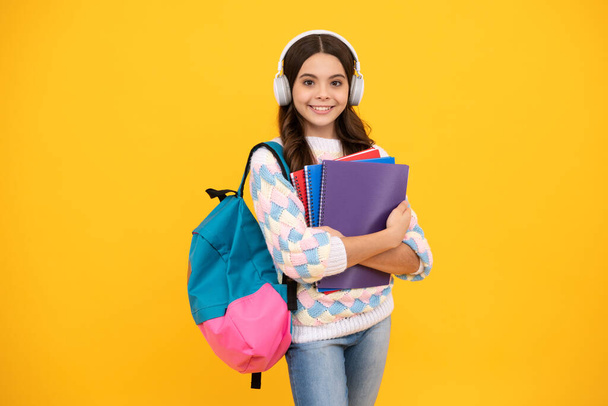 Schulmädchen, Teenager mit Kopfhörern halten Bücher auf gelbem, isoliertem Studiohintergrund. Schul- und Musikpädagogisches Konzept - Foto, Bild