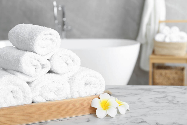 Rolled bath towels and beautiful flowers on white marble table in bathroom, space for text - Φωτογραφία, εικόνα