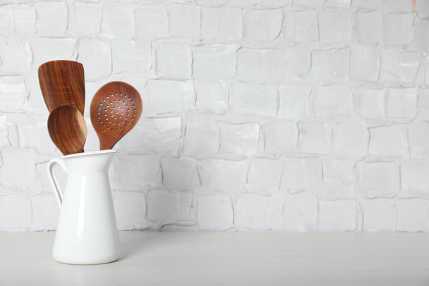 Set of wooden kitchen utensils in jug on table near white wall. Space for text - Photo, Image