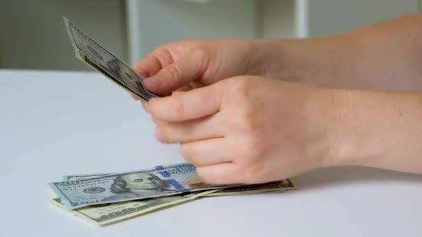 Μια γυναίκα μετράει χαρτονομίσματα των 100 δολαρίων σε λευκό φόντο. - Πλάνα, βίντεο