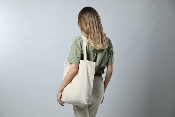 Woman with blank eco friendly bag on light background, back view - Foto, imagen