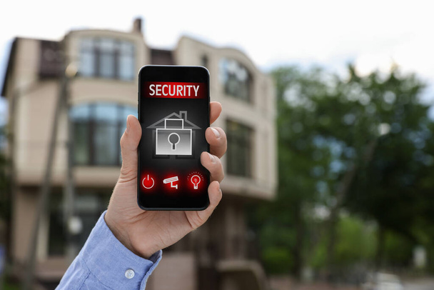 Man using home security application on smartphone in front of house outdoors, closeup - Fotoğraf, Görsel