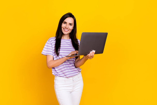 Photo of nice lovely pretty girl with long hairdo dressed striped t-shirt hold laptop typing email isolated on yellow color background. - Φωτογραφία, εικόνα