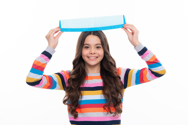 Child with long hair holding comb hairbrush for combing, beauty. Conditioner shampoo hair. Beauty kids salon. Child hairstyle. Happy girl face, positive and smiling emotions - Photo, image