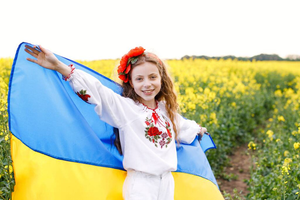 Pray for Ukraine. Child with Ukrainian flag in rapeseed field. Girl holding national flag praying for peace. - Φωτογραφία, εικόνα
