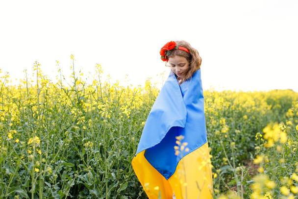 Ukrayna için dua et. Kolza tarlasında Ukrayna bayrağı taşıyan bir çocuk. Ulusal bayrak tutan kız barış için dua ediyor. - Fotoğraf, Görsel