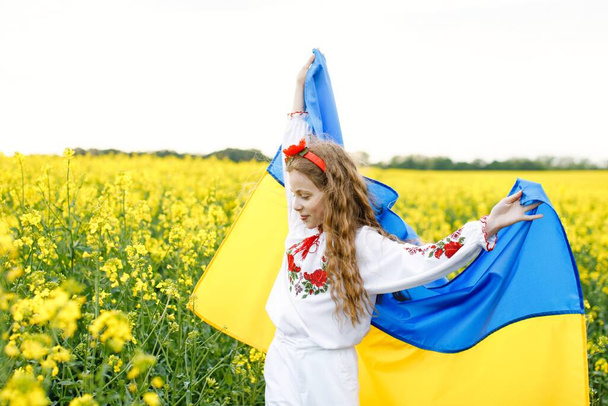 Pray for Ukraine. Child with Ukrainian flag in rapeseed field. Girl holding national flag praying for peace. - Фото, зображення