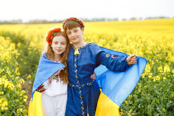 Pray for Ukraine. Two cute girls holding in hands a blue and yellow Ukrainian national flag in the middle of a rapeseed field - Foto, immagini