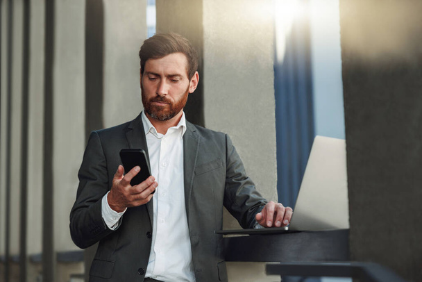 Attractive businessman with phone standing near office building . Business concept - Foto, immagini