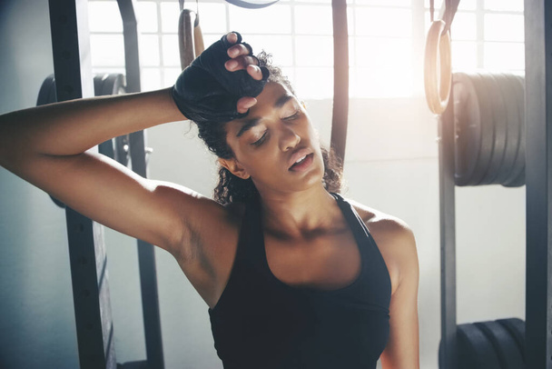 Tired but not defeated. a young sportswoman tired and wiping sweat off her forehead at the gym - Foto, immagini