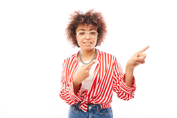 Positive kazakh girl with afro hairstyle points forefinger at copy space isolated on white studio background - 写真・画像