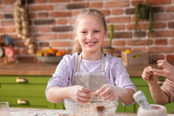 Happy smiling cute girls at the kitchen island take the kitchen apron and preparing the dough the delicious biscuits they spending wonderful time together. - Zdjęcie, obraz