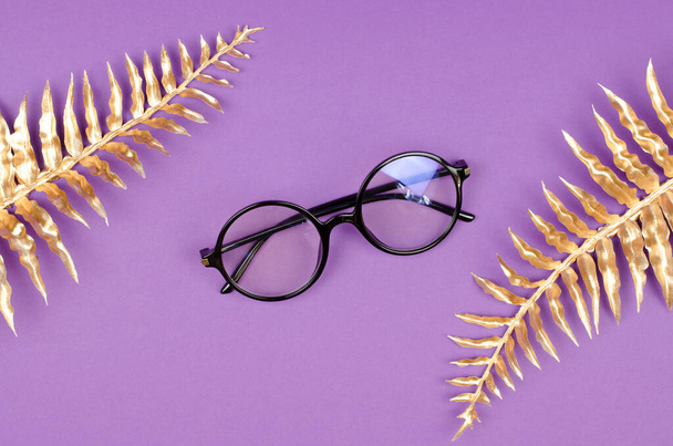 Stylish female glasses on a purple background with golden palm leaves. Glasses advertising mockup - Fotoğraf, Görsel