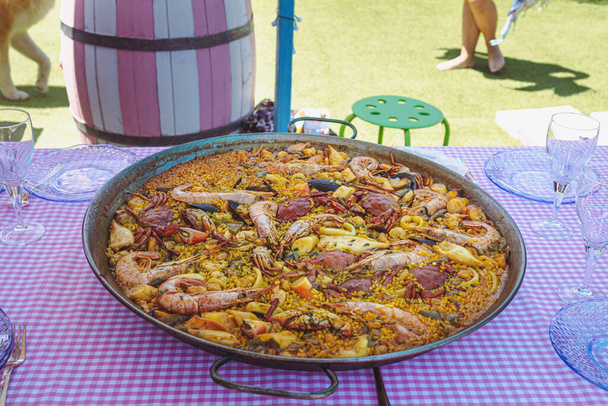 Traditional paella for the whole family. Outdoor dining with the family in the summer. Delicious traditional paella of Spanish cuisine - Foto, Imagen
