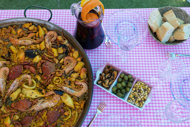 Traditional paella for the whole family. Outdoor dining with the family in the summer. Delicious traditional paella of Spanish cuisine - Photo, image