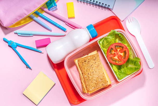 Healthy school meal, back to school concept. Children packed lunch box with balanced diet snack food - yogurt, cereal toast sandwich, apple, fresh vegetable salad, high-colored bright background - Foto, Imagen