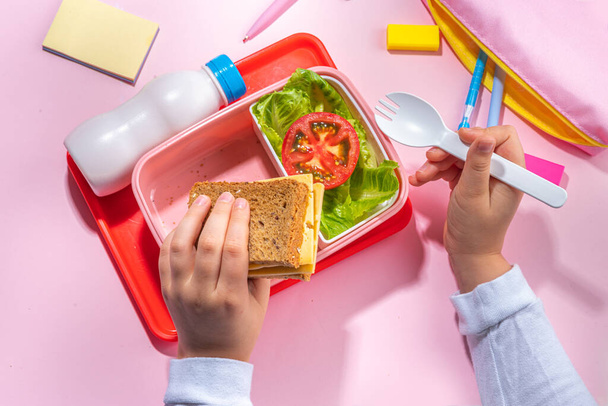 Healthy school meal, back to school concept. Children packed lunch box with balanced diet snack food - yogurt, cereal toast sandwich, apple, fresh vegetable salad, high-colored bright background - Photo, Image