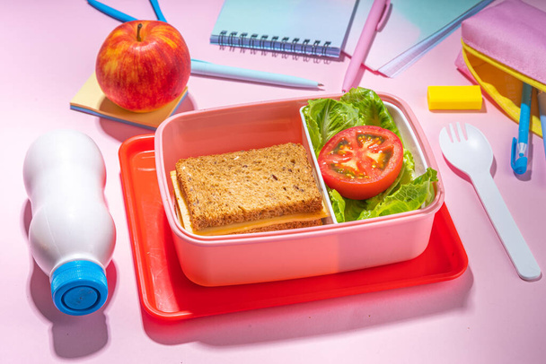 Healthy school meal, back to school concept. Children packed lunch box with balanced diet snack food - yogurt, cereal toast sandwich, apple, fresh vegetable salad, high-colored bright background - Foto, imagen