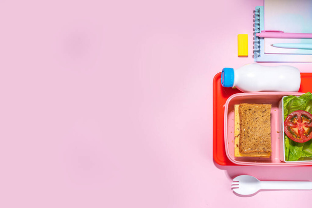 Healthy school meal, back to school concept. Children packed lunch box with balanced diet snack food - yogurt, cereal toast sandwich, apple, fresh vegetable salad, high-colored bright background - Foto, Bild
