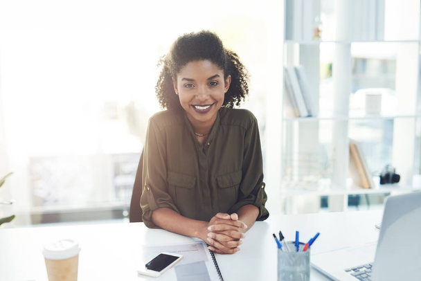 Welcoming you to another year of success and prosperity. Portrait of a confident young businesswoman sitting at her desk in a modern office - Foto, Imagen