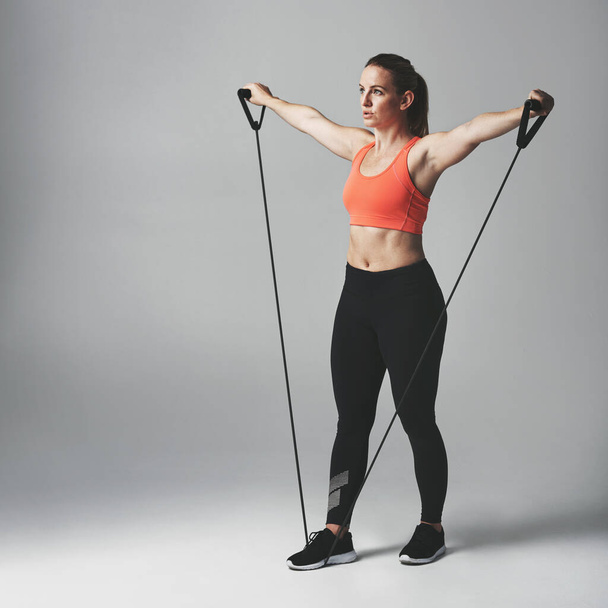 Resistance training is good for the whole body. Studio shot of an athletic young woman working out with a resistance band against a grey background - 写真・画像