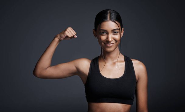 Strong is definitely the new beautiful. Studio portrait of a young sportswoman flexing her bicep against a gray background - Photo, image