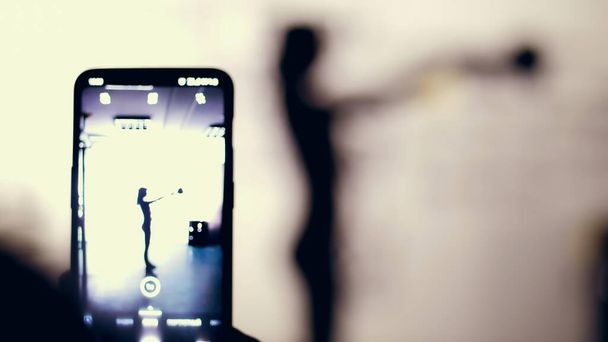 close-up, smartphone monitor, shooting a dark figure, outline of a woman performs exercising with weight. Muscular woman doing cross fit workout at gym. Fitness class cardio workout. - Φωτογραφία, εικόνα